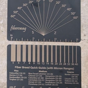 May include: A black metal tool with a protractor and a fibre breed quick guide. The protractor has markings for 0 to 60 degrees. The fibre breed quick guide lists different breeds of sheep with their micron ranges. The tool is labelled "fiberswag".