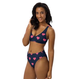 May include: A dark blue bikini set featuring a repeating pattern of small pink hearts. The top is a scoop-neck style with wide straps, and the bottom is a high-waisted design with a high-cut leg opening, providing full coverage for the wearer.