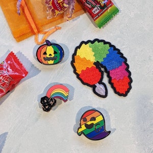 Puede incluir: Un conjunto de cinco pines de esmalte con un dise&ntilde;o de arco&iacute;ris. Los pines incluyen una calabaza, un arco&iacute;ris con un dado negro, un arco&iacute;ris con una cola, un fantasma arco&iacute;ris y un gusano arco&iacute;ris.