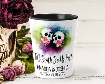 May include: A white shot glass with a black rim, decorated with two skulls and pink flowers. The text "Till Death Do Us Part" is visible, along with names and a date. The background features watercolour splashes of green, purple, and blue.