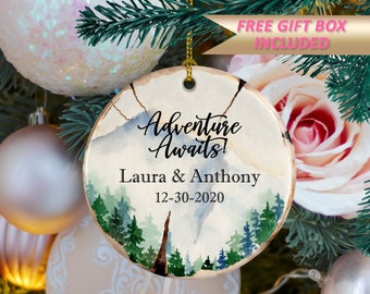 Może przedstawiać: Okrągła, rustykalna ozdoba choinkowa z napisem "Adventure Awaits!" oraz imionami "Laura & Anthony" i datą "12-30-2020". Ozdoba ma akwarelowy wzór gór i drzew.