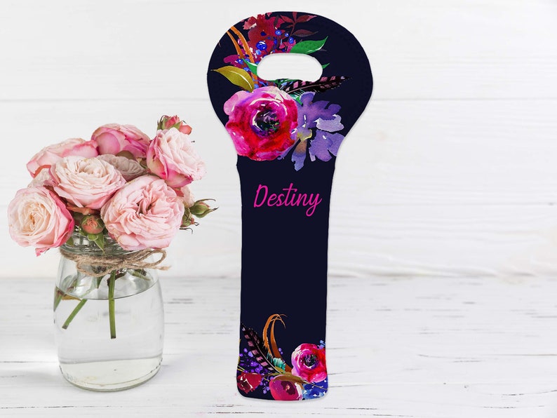 May include: A navy blue wine bottle bag with a floral design featuring pink and purple flowers, green leaves, and feathers. The word "Destiny" is written in pink script. A bouquet of pink roses in a glass jar is in the background.