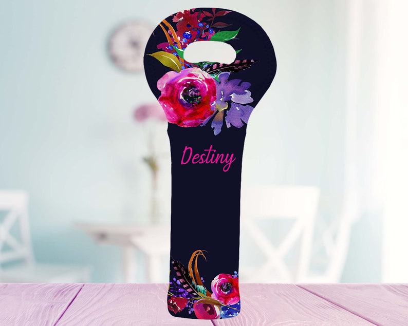 May include: A navy blue wine bottle bag with a floral design featuring pink and purple flowers, berries, and feathers. The word "Destiny" is written in pink script. The bag has a handle at the top.