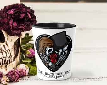 May include: A white shot glass with a black rim features a heart-shaped graphic of a skeleton couple embracing, holding a red rose. The text "Till Death Do Us Part" and names are below the graphic. A skull and flowers are in the background.