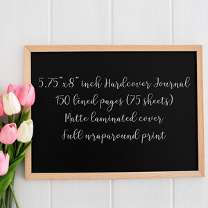 May include: A black hardcover journal with a wooden frame, measuring 5.75" x 8". The journal has 150 lined pages, a matte laminated cover, and a full wraparound print. A bouquet of pink and white tulips is in the lower left corner.