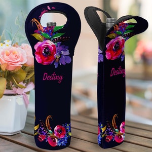 May include: A black wine bottle tote with a floral design featuring red and purple flowers, green leaves, and gold feathers. The word "Destiny" is written in pink script. The tote has a handle at the top.