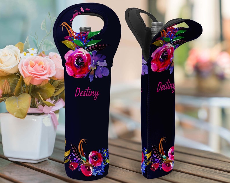 May include: A black wine bottle tote with a floral design featuring red and purple flowers, green leaves, and gold feathers. The word "Destiny" is written in pink script. The tote has a handle at the top.