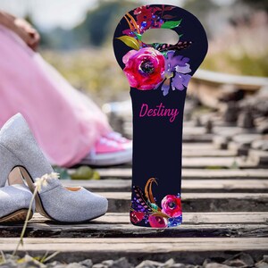 May include: A navy blue wine bottle bag with a floral design and the word "Destiny" in pink. The bag features red, purple, and blue flowers. Silver glitter high heels are in the foreground.