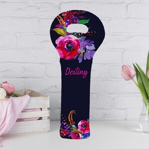 May include: A navy blue wine bottle bag with a floral design. The bag features a large pink rose and other flowers in shades of red, purple, and yellow. The word "Destiny" is written in pink script.