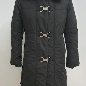 May include: Black quilted coat with a wide collar and silver-tone metal clasps. The long coat features a tailored design with vertical stitching and a mid-thigh length. The coat is displayed on a mannequin.