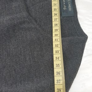 Puede incluir: Primer plano de un su&eacute;ter gris oscuro con una cinta m&eacute;trica al lado. El su&eacute;ter tiene una etiqueta que dice "FALCONERI made in Italy". La cinta m&eacute;trica muestra la longitud del su&eacute;ter en cent&iacute;metros.