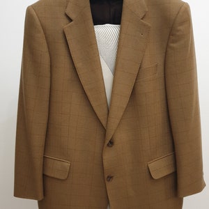Peut inclure: Un blazer marron à carreaux avec deux boutons de fermeture. Le blazer est suspendu à un cintre blanc avec un bouton noir.