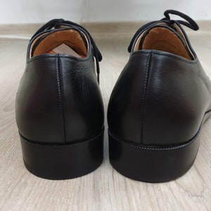 May include: A pair of black leather dress shoes with laces. The shoes have a rounded toe and a stitched seam around the sole.