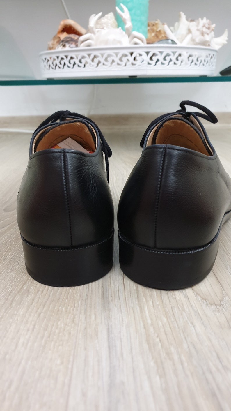 May include: A pair of black leather dress shoes with laces. The shoes have a rounded toe and a stitched seam around the sole.
