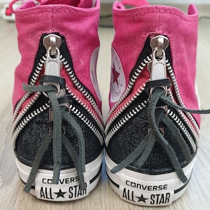 May include: A pair of black and pink Converse All Star high-top trainers with zipper detailing and black laces.