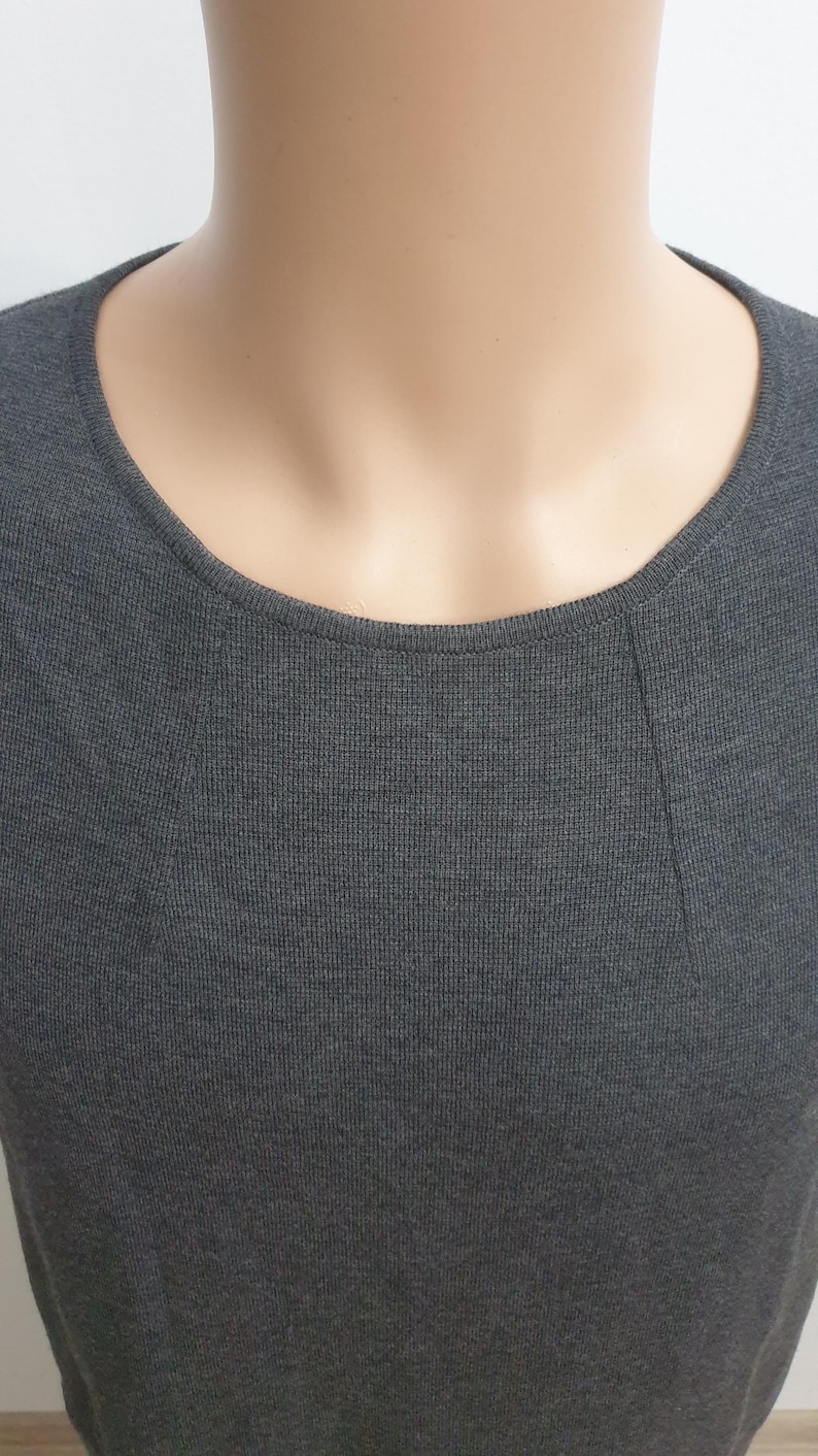 Puede incluir: Primer plano de un top de punto gris oscuro con cuello redondo. La tela tiene una fina textura acanalada. El top se muestra en un maniqu&iacute;, mostrando la forma y el ajuste de la prenda. El estilo es sencillo y vers&aacute;til.