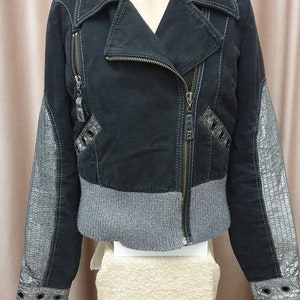 May include: A black denim jacket with silver accents on the sleeves and a gray knit band at the waist. The jacket has a zipper closure and a collar.