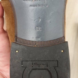 May include: Close-up of the bottom of a brown suede shoe with a black leather sole. The shoe is labelled "Salvatore Ferragamo" and "Made in Italy". The size is marked as "7 EE".