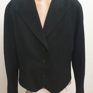 Puede incluir: Un blazer negro con solapa de muesca y cierre de tres botones. El blazer tiene un corte entallado y un diseño clásico, adecuado para diversas ocasiones. La chaqueta se muestra en un maniquí.