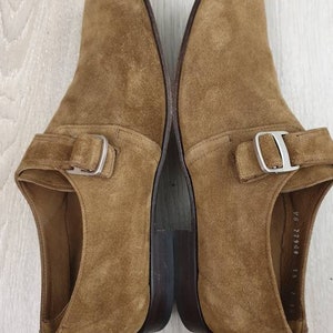 May include: A pair of brown suede shoes with a single buckle strap. The shoes have a dark brown leather sole.