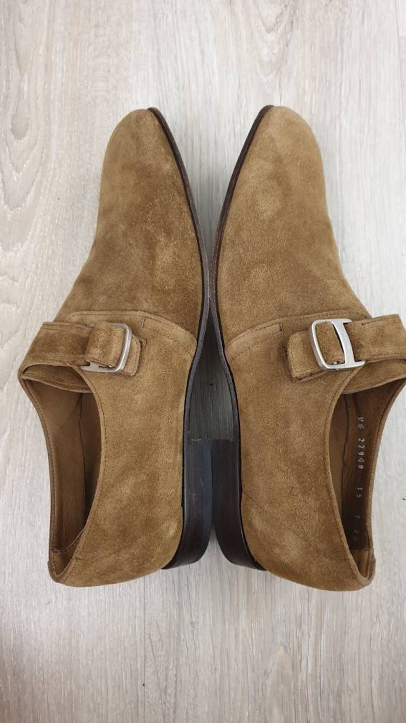 May include: A pair of brown suede shoes with a single buckle strap. The shoes have a dark brown leather sole.