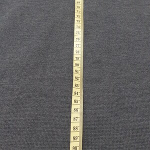 Puede incluir: Una tela gris oscuro se muestra con una cinta m&eacute;trica amarilla. La cinta est&aacute; marcada en cent&iacute;metros, con n&uacute;meros del 63 al 95. La tela es de color gris oscuro liso.