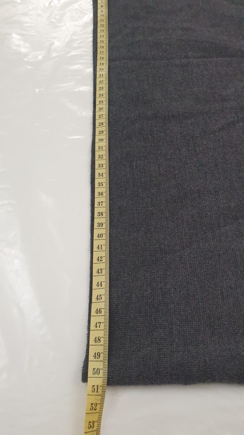 Puede incluir: Una muestra de tela gris oscuro junto a una cinta m&eacute;trica. La cinta muestra medidas de hasta 135 cm. La tela parece ser de color liso y tiene una superficie ligeramente texturizada.