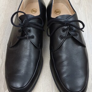 May include: A pair of black leather lace-up shoes with a rounded toe. The shoes have a subtle textured finish and a simple design.