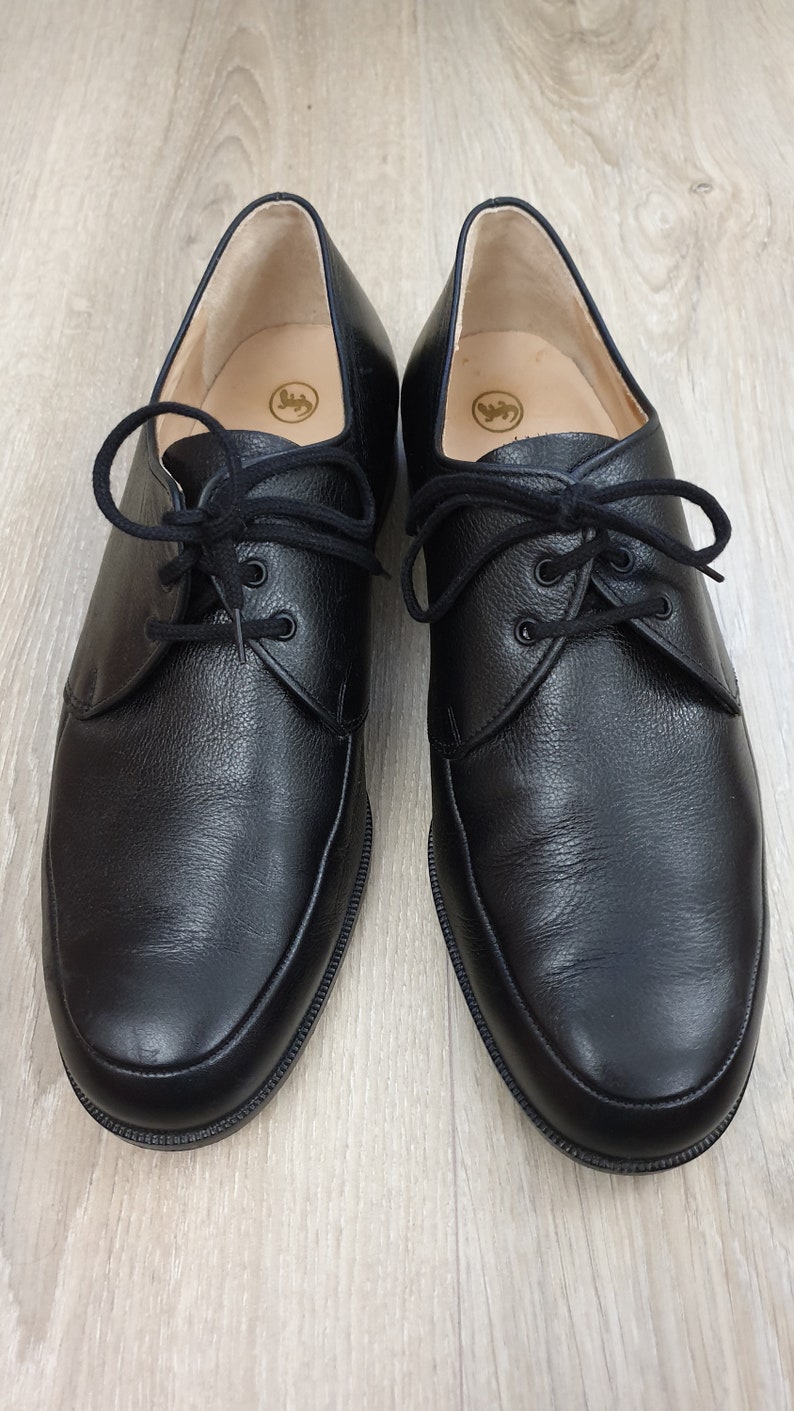May include: A pair of black leather lace-up shoes with a rounded toe. The shoes have a subtle textured finish and a simple design.