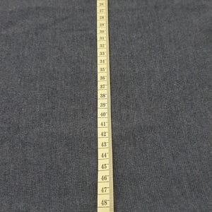 Puede incluir: Primer plano de una tela gris con una cinta m&eacute;trica amarilla. La cinta est&aacute; marcada con n&uacute;meros de 33 a 137 cm, proporcionando una referencia visual de longitud y medici&oacute;n.