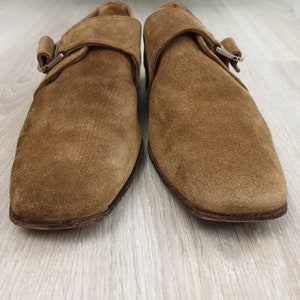 May include: A pair of brown suede buckle shoes with a pointed toe. The shoes have a single buckle strap across the top of the foot.