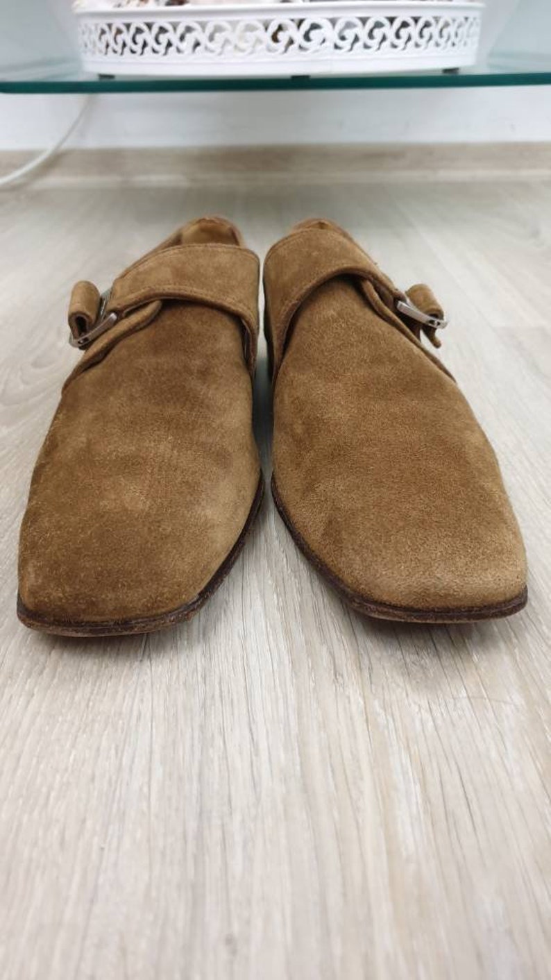 May include: A pair of brown suede buckle shoes with a pointed toe. The shoes have a single buckle strap across the top of the foot.