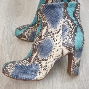 Op de afbeelding: Blauwe, groene en bruine slangenleren enkellaarsjes met een blokhak.