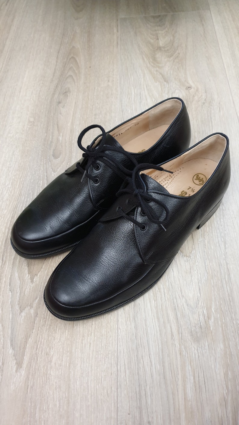 May include: A pair of black leather lace-up shoes with a rounded toe. The shoes have a simple design and are made of high-quality leather.