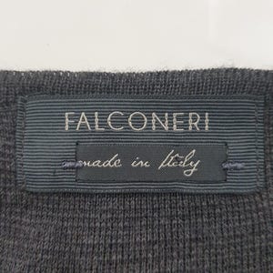 Puede incluir: Primer plano de una tela de punto gris oscuro con una etiqueta rectangular. La etiqueta, en un tono de gris m&aacute;s oscuro, dice "FALCONERI" en may&uacute;sculas, con "made in Italy" debajo.