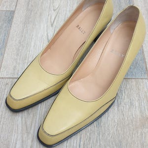 Può includere: Un paio di décolleté Bally giallo pallido con punta e tacco basso. Le scarpe hanno un bordo nero e il logo Bally è visibile all'interno. Le scarpe sono in pelle e in buone condizioni.