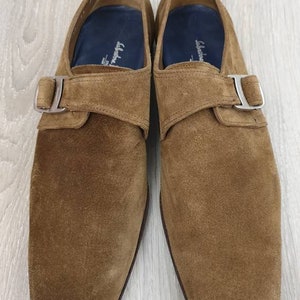 May include: A pair of brown suede monk strap shoes with silver buckles. The shoes have a square toe and a low heel.