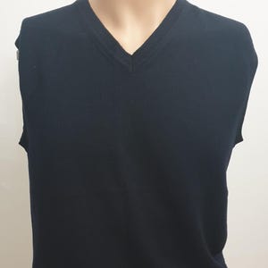 May include: A navy blue V-neck vest displayed on a mannequin. The sleeveless garment has a ribbed neckline and a simple, classic design. The vest is made of a soft, likely knit, material.