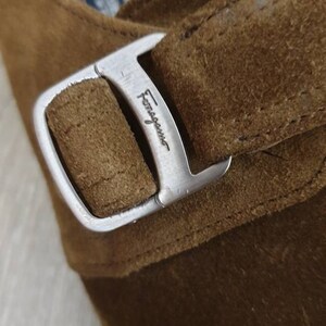 May include: Close-up of a brown suede shoe with a silver buckle. The buckle has the word "Ferragamo" engraved on it.