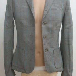 May include: A grey plaid blazer with a notched collar, two front pockets, and three buttons. The blazer features a subtle blue accent in the plaid pattern. The garment is displayed on a mannequin.