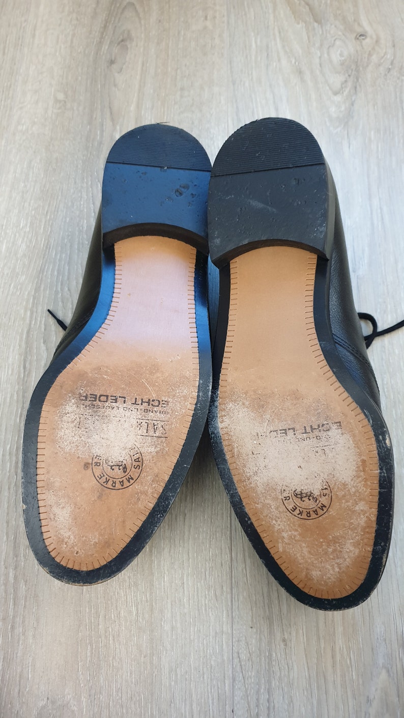 May include: Close-up of the soles of two black leather shoes. The soles are brown and have the text "MARKE" and "ECHT LEDER" printed on them.