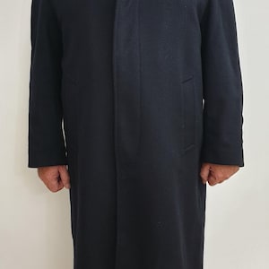 May include: A long, dark navy blue coat with a classic collar and a straight, tailored fit. The coat has a simple, elegant design, with a subtle texture and a knee-length hemline. The coat is suitable for various occasions.