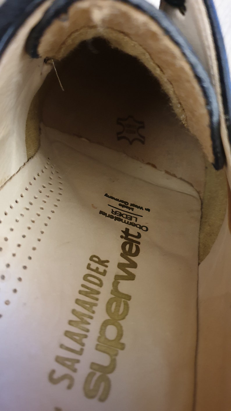 May include: Close-up of the inside of a white shoe with gold lettering that reads "Superweit" and "Salamander" with the words "OBERWEITE" and "LEDER" in smaller font. The shoe is made of leather.