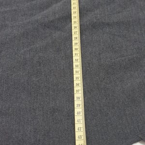 Puede incluir: Una tela gris con una cinta m&eacute;trica que corre verticalmente por el lado derecho. La cinta est&aacute; marcada en cent&iacute;metros, mostrando medidas de 1 a 49 cm. La tela parece ser un material de punto.