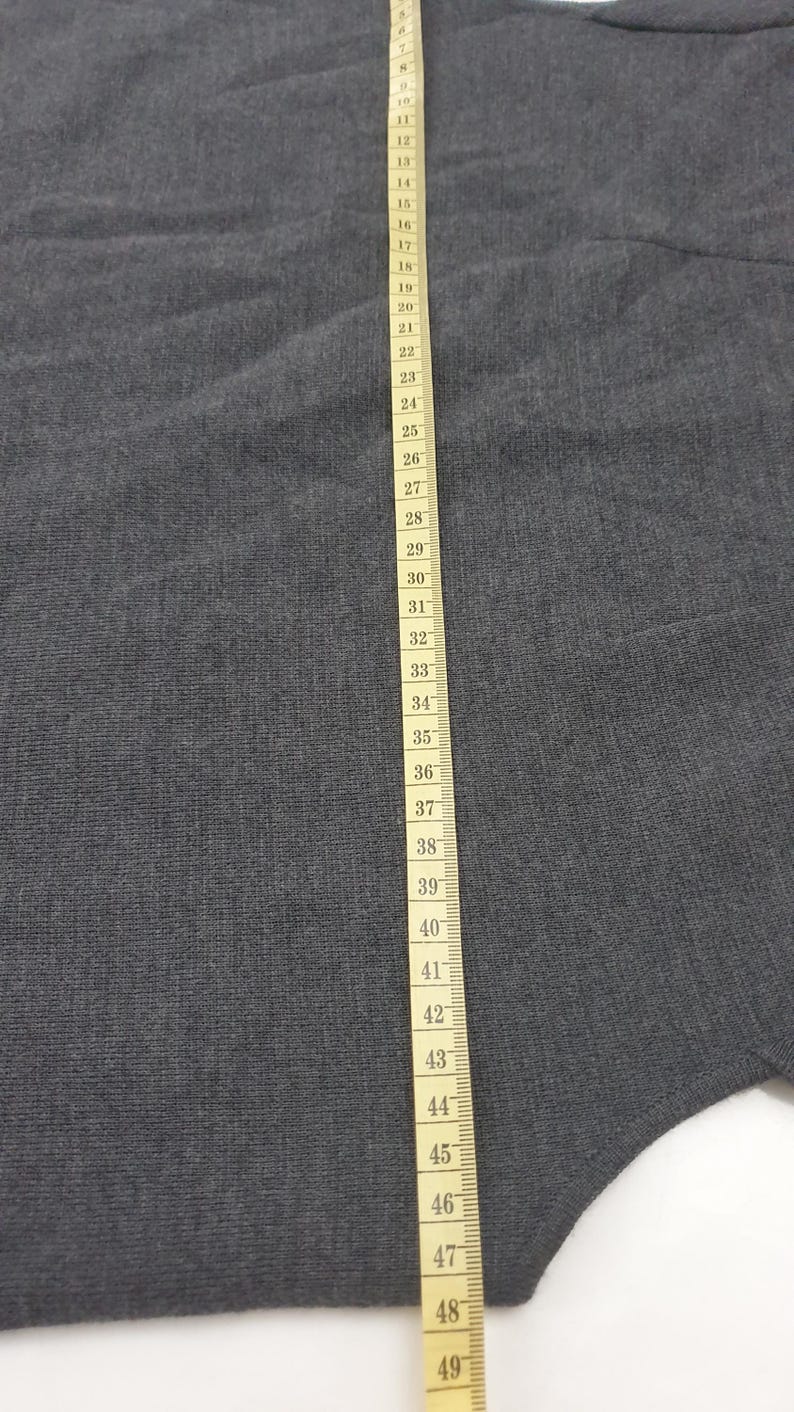 Puede incluir: Una tela gris con una cinta m&eacute;trica que corre verticalmente por el lado derecho. La cinta est&aacute; marcada en cent&iacute;metros, mostrando medidas de 1 a 49 cm. La tela parece ser un material de punto.