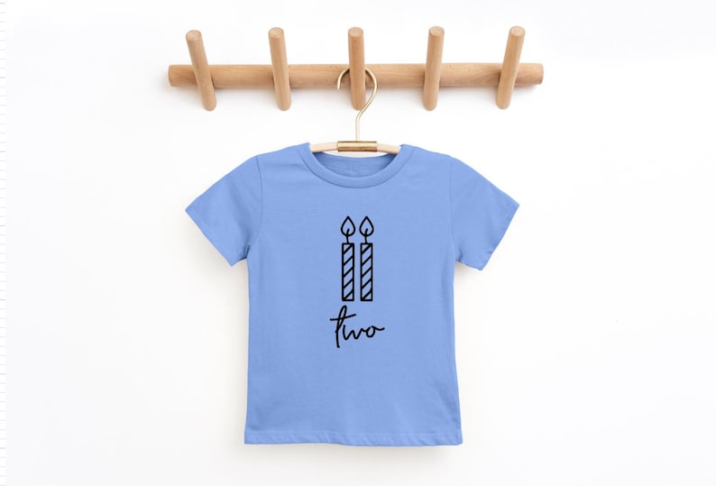 May include: A light blue t-shirt with a black graphic of two candles and the word "two" written in cursive.