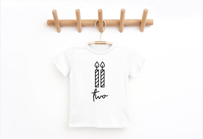 May include: White t-shirt with a black graphic of two birthday candles and the word "two" written in cursive.
