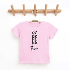 May include: Pink short-sleeved t-shirt with a black graphic of two candles and the word "two" written in cursive.