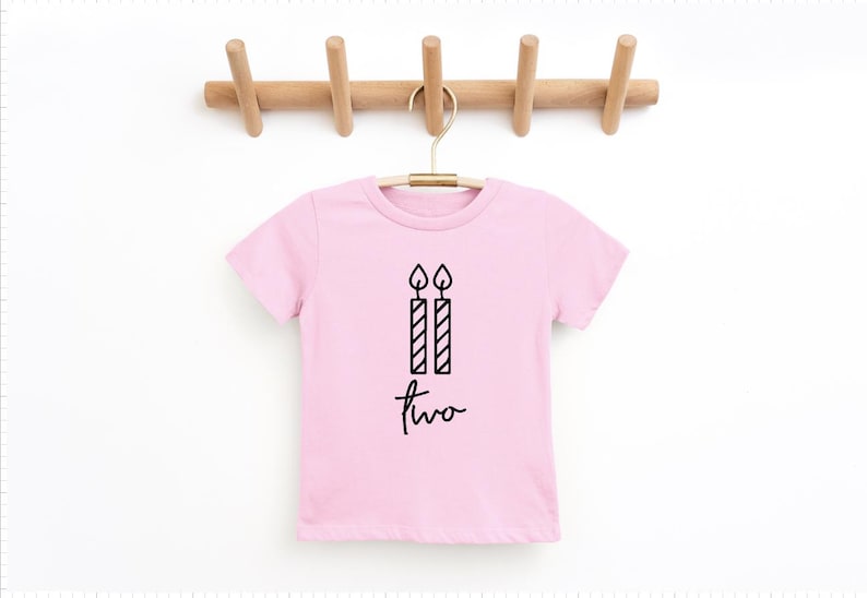 May include: Pink short-sleeved t-shirt with a black graphic of two candles and the word "two" written in cursive.