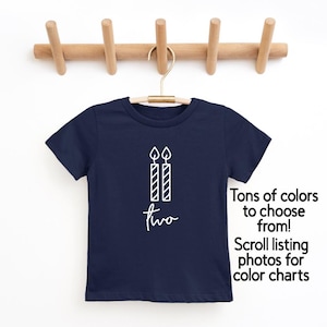 May include: Navy blue t-shirt with a white graphic of two candles and the word "two". The text "Tons of colors to choose from! Scroll listing photos for color charts" is also visible.